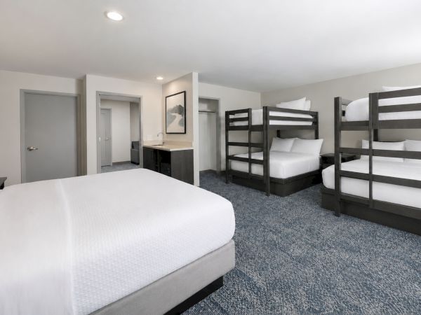 A bright hotel room with white beds, bunk beds, and a small bathroom vanity in the background.
