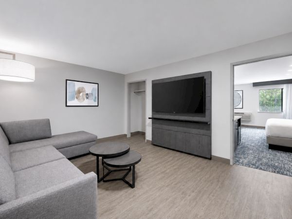 Modern living room with gray sofa, round coffee tables, flat-screen TV on a dark console, and framed wall art.
