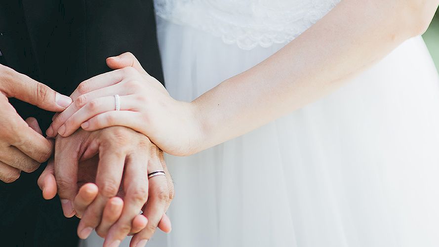 Two hands with rings join in a wedding moment, a bride and groom holding each other&rsquo;s fingers.