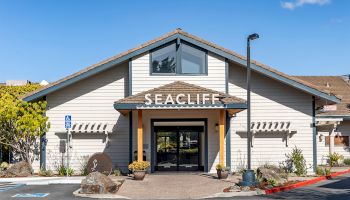 Front of a building with the sign &ldquo;SEACLIFF,&rdquo; plus a parking sign, landscaped entrance, and a clear blue sky.
