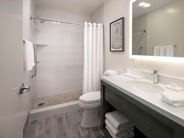 Modern bathroom with a glass shower, white towels, and a vanity sink with toiletries.