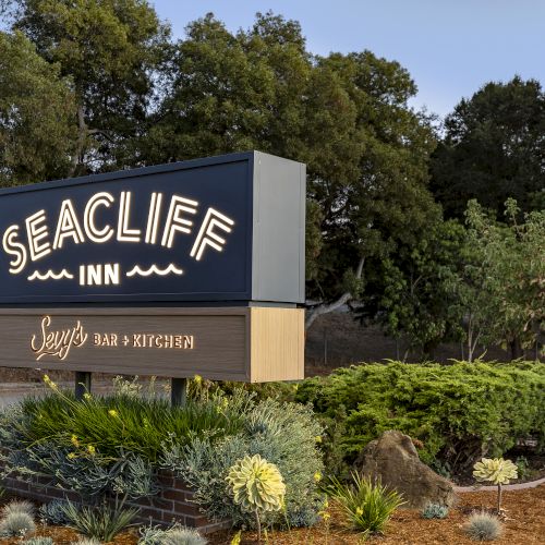 A sign reading &ldquo;Seacliff Inn&rdquo; with &ldquo;Bar + Kitchen,&rdquo; lit up against a backdrop of trees and landscaping.