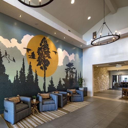 An indoor lobby with a large wall mural (trees and sun), blue sofas, and a hanging chandelier with lit candles.