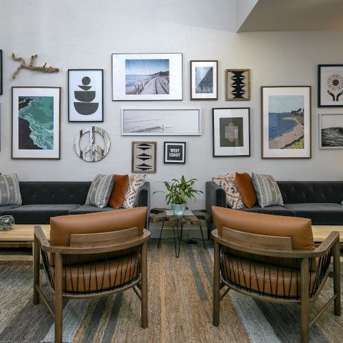 A cozy living room with a dark sectional, wooden coffee table, plants, and a gallery wall of ocean-themed framed art.