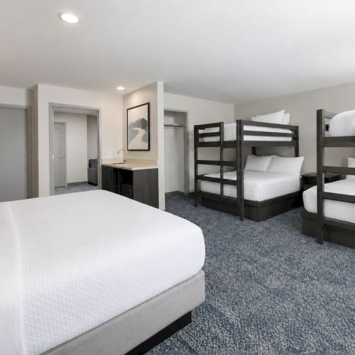 A bright hotel room with multiple beds, including bunk beds, plus a bathroom vanity visible in the background.