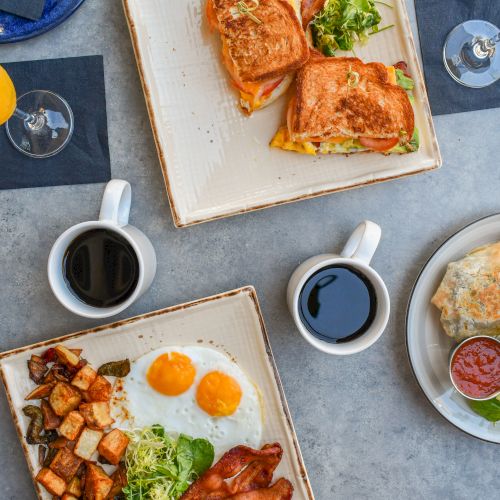 A brunch spread with open-faced sandwiches, omelet, roasted potatoes, salads, and coffee, plus orange juice.